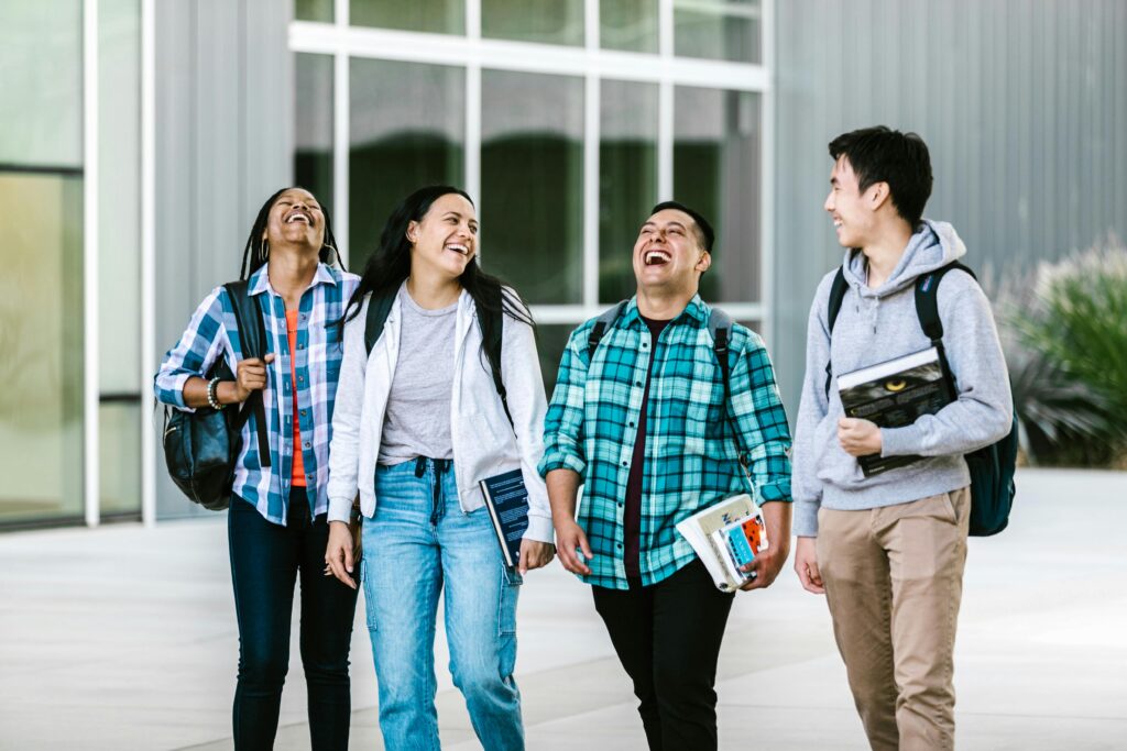 Group of diverse college students laughing and walking together on campus with backpacks and books