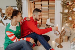 A couple sitting by a Christmas tree, lighting candles together during the holidays, sharing a calm and tender moment.
