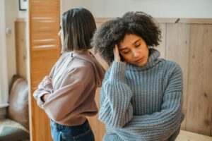 Two women sitting back-to-back in emotional distress, illustrating relationship conflict, emotional disconnection, and commitment struggles in modern dating.