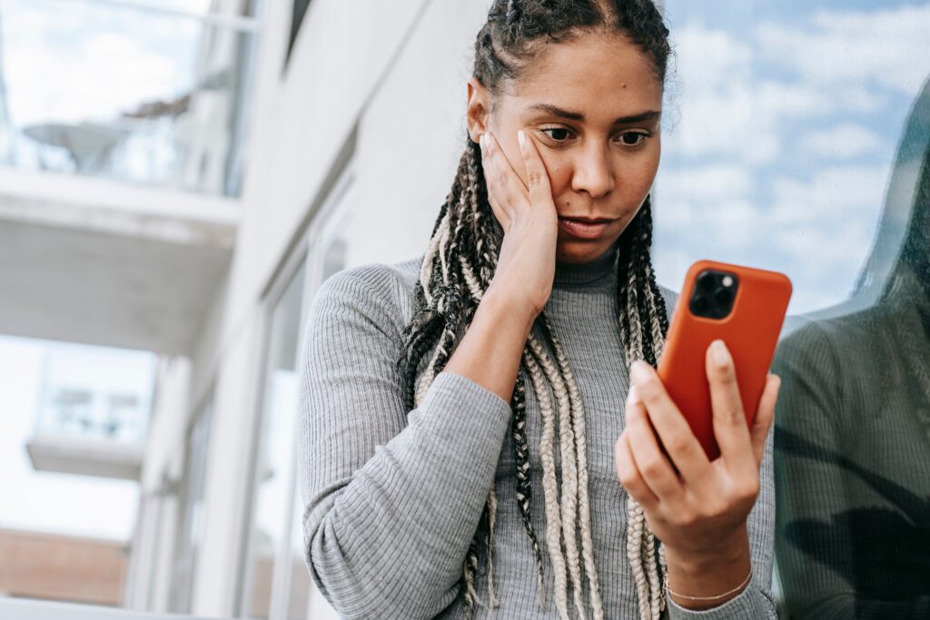 Woman with braided hair resting her hand on her cheek while anxiously looking at her phone, reflecting the overthinking and uncertainty common in a situationship