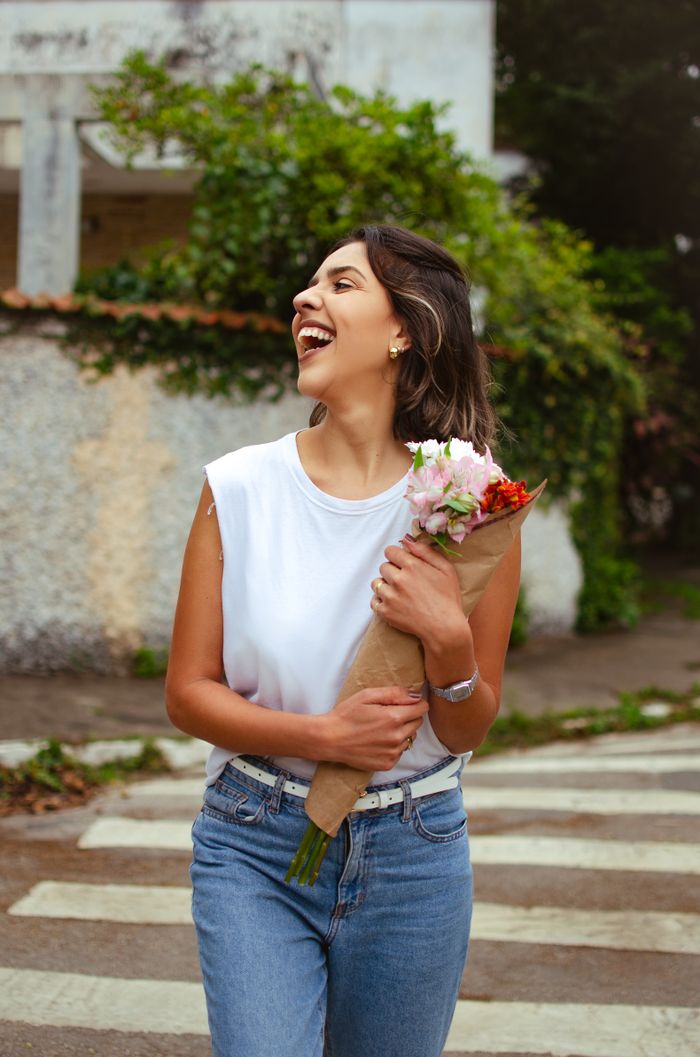 Happy woman in casual outfit walking outdoors with a bouquet of flowers, embodying a joyful summer vibe.